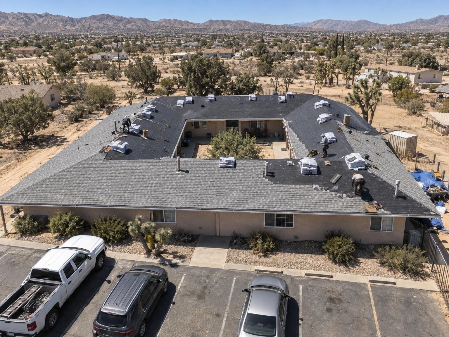 Top-down drone view of a large U-shaped building mid re-roof, new shingles going on